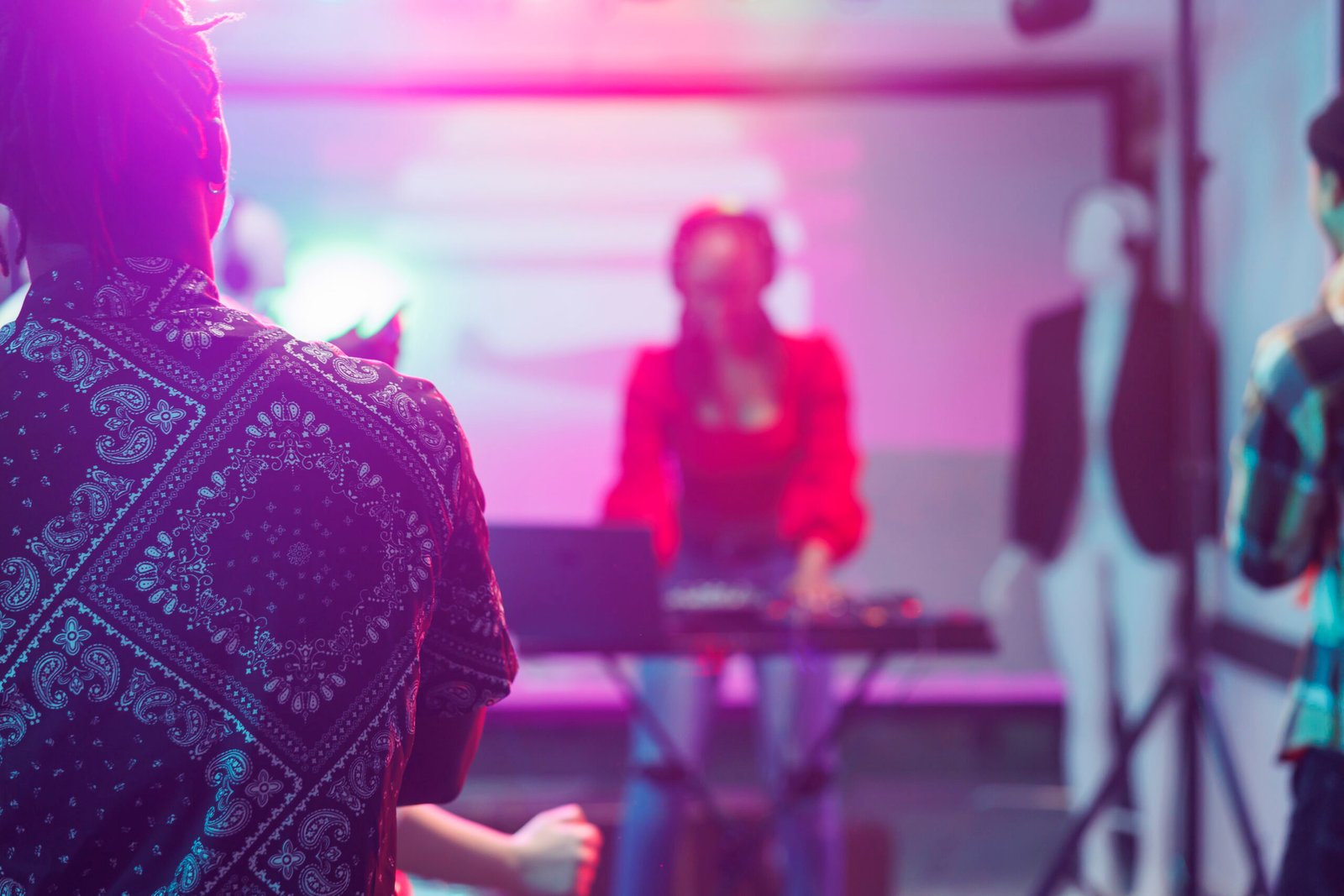 People watching live electronic music concert on stage with spotlights in nightclub. African american musician performing using dj controller in nightclub on blurred background